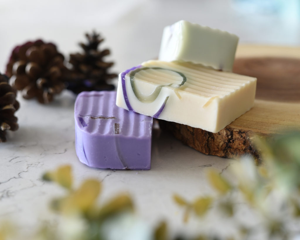 Mini Lifestyle Tabletop Photo of purple and cream handmade soap with pinecones and wood