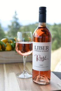 Mini Lifestyle Tabletop Photo of a table and a bottle, glass of rose wine, background blurry Okanagan vineyards and fruit basket
