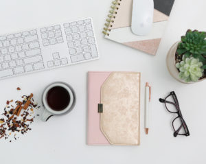 Tabletop photo of pink office supplies, computer keyboard, mouse, glasses, pen, coffee and plant