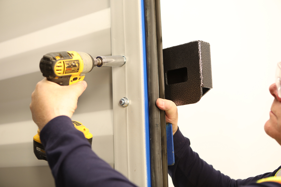 Lifestyle photo for guide book of man in yellow vest drilling door of a blue steel box
