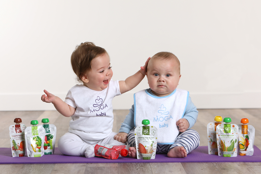 Lifestyle photo of 2 babies sitting on a purple yoga mat with baby snacks and drinks
