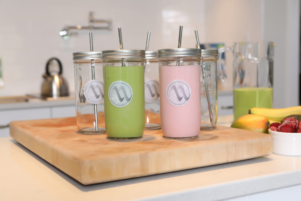 Mini lifestyle photo of green and pink smoothies in mason jars on kitchen counter top