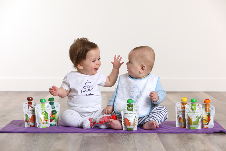 Lifestyle photo of 2 babies sitting on a purple yoga mat with baby snacks and drinks